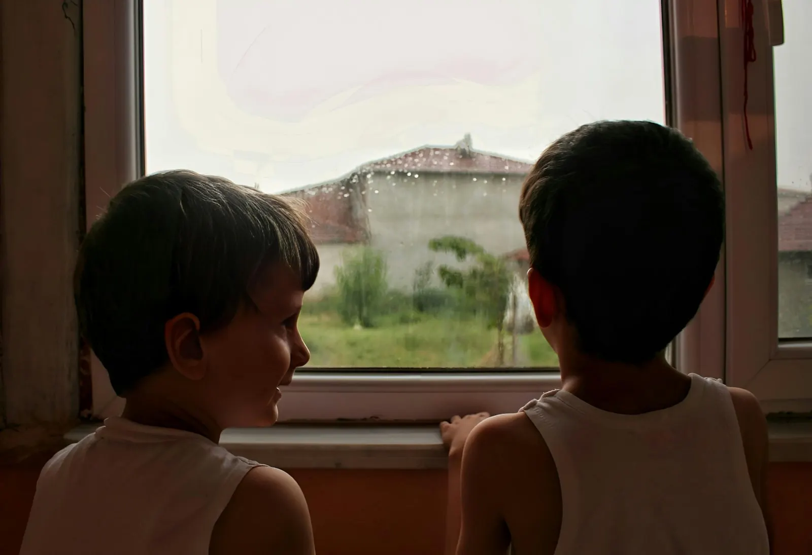 Dos niños mirando por la ventana un día gris